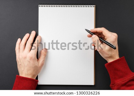 open notebook with black pen in hands on black background top view, school notepad and male hands in a red jacket on a dark table, a desktop in the office