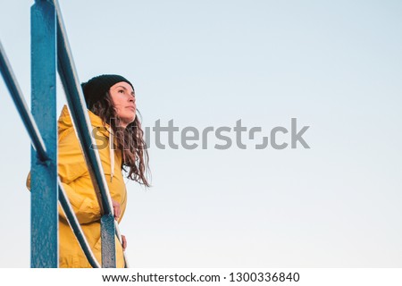 Portrait of a young brunette woman on a lifeguard tower wearing a yellow  raincoat and hat. Looking at the horizont.