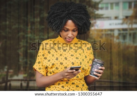 Young african woman dressed in yellow casual clothes talking by her phone, blurred background