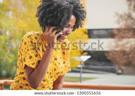 Young african woman dressed in yellow casual clothes talking by her phone, blurred background