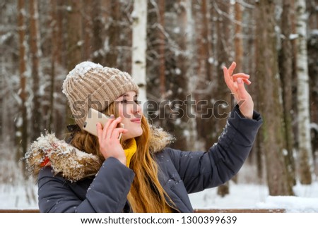 smiling girl in winter park greets someone with her hand while talking on the phone