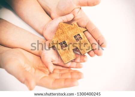 child's and woman's hands holds wooden flat house on the white background