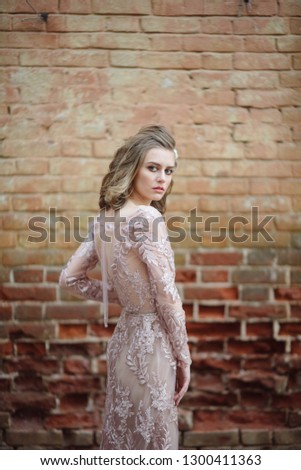 Young woman stands by the brick wall in a dress