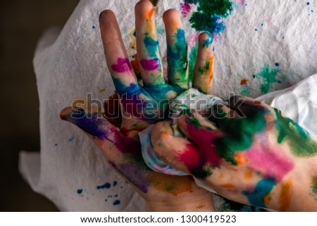 A child cleans up hands that are covered in red, pink, yellow, orange, red, blue, green, and purple paint