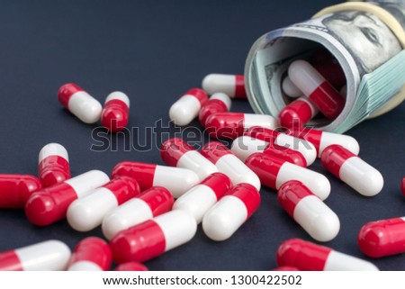 biotech and pharmaceutical companies. red white pills spill out of folded dollars, dark background