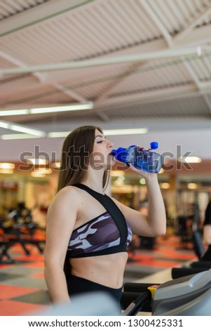 Gym woman working out drinking water smiling happy standing by moonwalker fitness machines. Beautiful fit young mixed race Caucasian Chinese Asian female fitness model inside in fitness center.