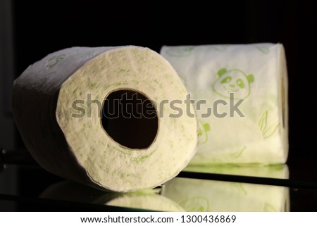 A roll of toilet paper white with green pandas. Dark background. Lavender and mirror. Bathroom