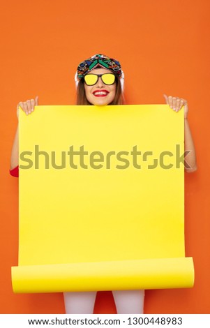 young and hipster girl presenting an yellow empty roll of papper, space for text, on orange background