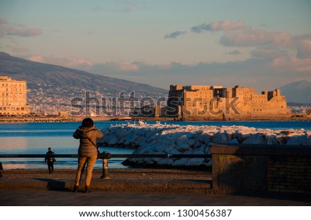 Woman taking a picture of View of the coast in Naples and medieval Castel dell'Ovo Sunset time. Egg castle. Panorama.
