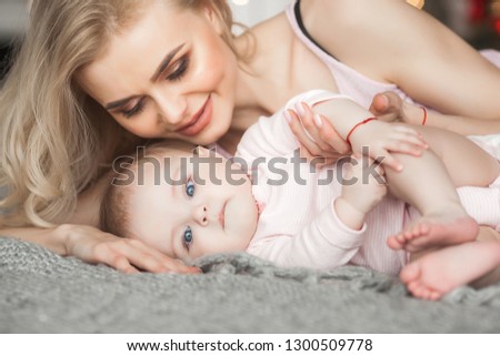 Young mother taking care of her little baby girl. Beautiful mom and her daughter indoors in the bedroom. Loving family. Attractive mum holding her child.