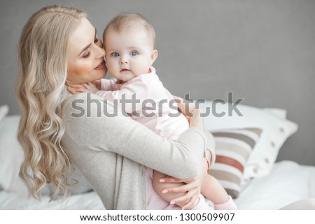 Young mother taking care of her little baby girl. Beautiful mom and her daughter indoors in the bedroom. Loving family. Attractive mum holding her child.