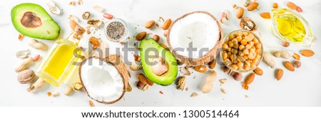 Healthy vegan fat food sources, omega3, omega6 ingredients - almond, pecan, hazelnuts, walnuts, olive oil, chia seeds, avocado, coconut, dark green background copy space Royalty-Free Stock Photo #1300514464