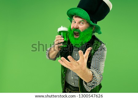 A smiling happy senior man in a leprechaun hat with green beer at studio. He celebrates St. Patrick's Day. The celebration, festive, beer, holiday, alcohol, party concept