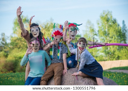 children in colorfull stylish Indian masks are sitting on a stone on a summer day in the park