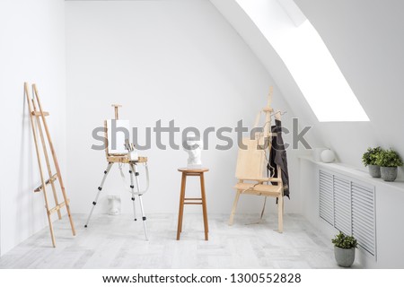 White and bright studio with a window and gray floor. Workspace of the artist. Easel, canvases and plaster figures for learning to draw. Conceptual interior without people.