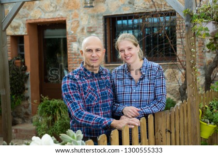 Portrait of positive spouses standing in backyard near wooden fence