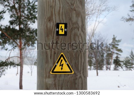 Electric shock sign on a wooden pillar of  medium voltage overhead cable line in snowy bacground