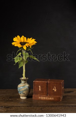 Happy Valentine's Day vintage wooden Perpetual calendar for February 14 on a black background and a sunflower in small marble vase