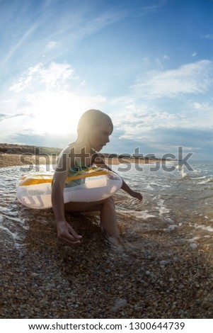 portrait, happy little girl swims in the sea on an inflatable circle, wide-angle landscape