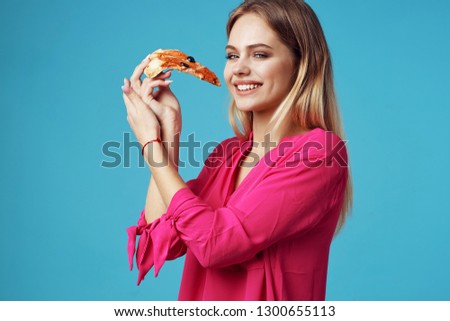 beautiful glamor woman in pink shirt eats pizza on blue isolated background