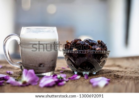 Close up shot of popular Indian & Asian Khajor dudh or dates milk in a transparent glass bowl along with raw dates on a brown colored surface or background.