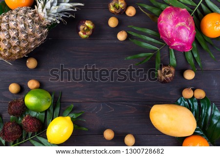 Tropical fruit frame with palm leaves on a dark wooden background, flat lay copy space