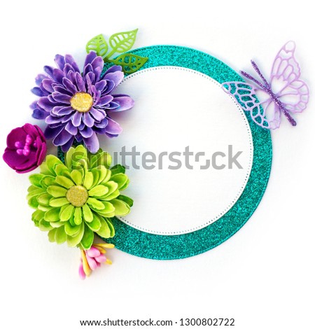 shiny turquoise frame with handmade paper flowers of light green and purple and purple paper butterfly on white background.

