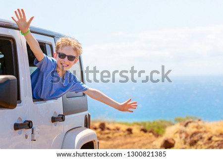 happy positive caucasian boy in sunglasses peeking out of the car window with his hands up in the air, tropical family vacation or active road trip concept, copy space on right