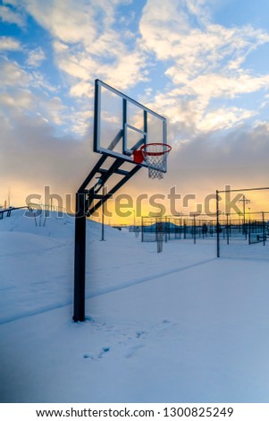 Snow covered outdoor basketball court at sunset
