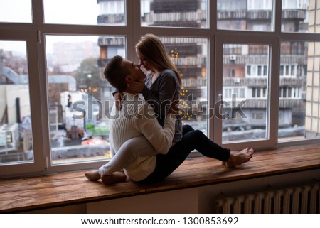 Couple kissing while sitting on window sill at home. Valentines Day. Love, happiness, people and fun concept. 