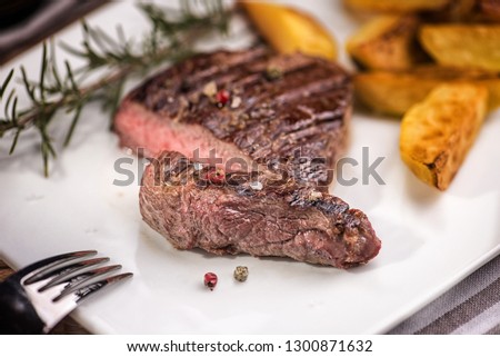Beef steak with fried potatoes in slices on a white rectangular plate in a restaurant.