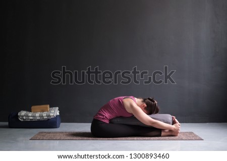 woman practicing yoga, doing Seated forward bend pose, using bolster. Royalty-Free Stock Photo #1300893460