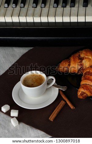 Still life with a white Cup of coffee, croissants and cinnamon on a retro piano background