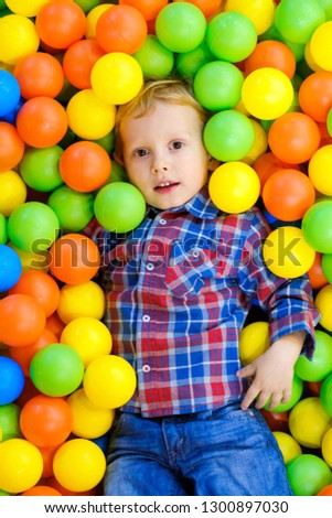 Happy child, kid boy playing, having fun on playground with colorful plastic balls in pool. Game center for family weekend, holiday party with kids, games area room. Entertainment center with toys.