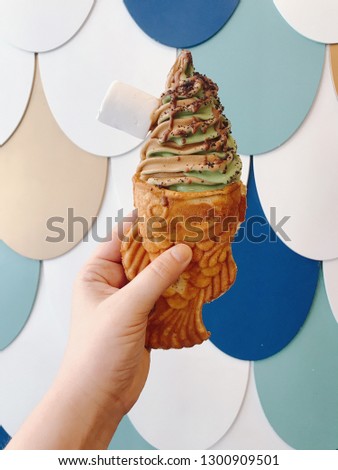 Hand with Fish shaped ice-cream with chocolate and mint creamy ice-cream on a colorful fish flakes background