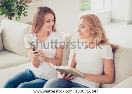 Close up photo of two people mum and teen daughter holding hands arms novel new telephone showing favorite app picture song wondering wear white t-shirts jeans sit on comfy sofa