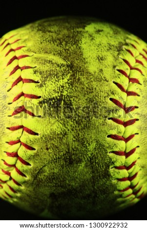 Yellow softball closeup with red seams on black background.