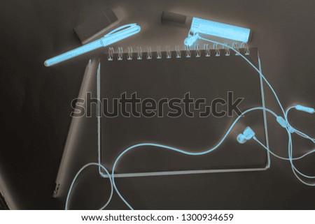 Negative snapshot of a notebook around which pens are pencils markers and headphones
