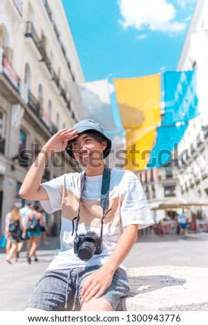 Asian guy with a camera sitting outdoors and smiling. Asian tourist traveling.
