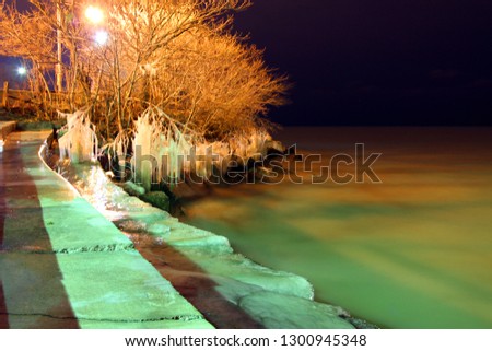 Night time greenish light over calm water, icy beach and frozen trees. 