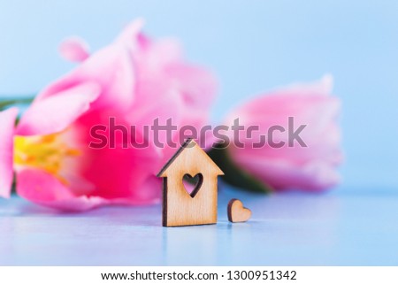 Wooden house with hole in form of heart with blurred flowers on background. Spring romantic composition.