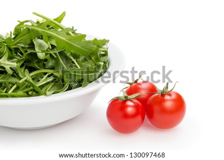 fresh rucola leaves in a bowl and tomatoes, isolated on white