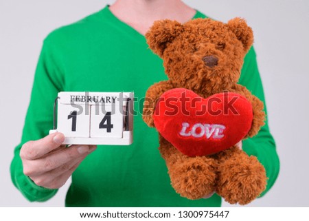 Hands of young man holding calendar block and teddy bear ready for Valentine's day