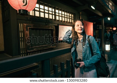 asian lady traveler holding slr camera carrying bag smiling searching for dinner restaurant in hanamikoji street in kyoto japan. young travel woman standing on dark road in gion at night red lantern