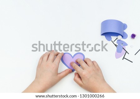 Child makes an Easter bunny out of paper. Children's hand. White background. Holiday Easter light. DIY purple hare.