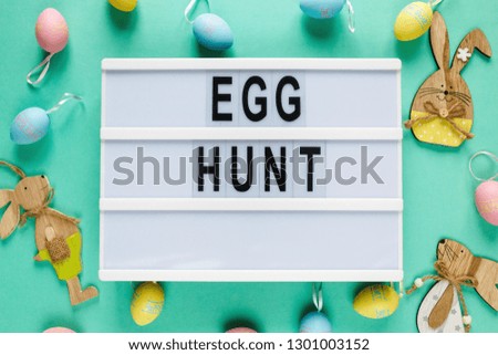 Happy Easter text on lightbox on green pastel paper background with yellow, pink, blue eggs and bunnies  Bright template for Easter, top view, flat lay, holiday background with copy space 