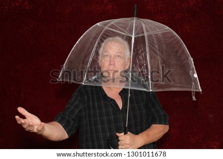 Man with umbrella. A man poses in a photo booth with a Burgundy Red Velvet Background with a clear umbrella. Room for text. 