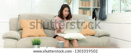 Attractive pretty young asian woman enjoying shopping on laptop paying with bank card, sitting on sofa in beautiful decoration living room, happy lifestyle with digital technology concept.