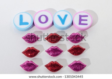 The word love made from rounded erasers and little red and purple lips against white background. Valentines Day decoration