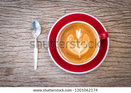coffee with milk making for flower picture in red cup on plate and spoon put on bark wooden table